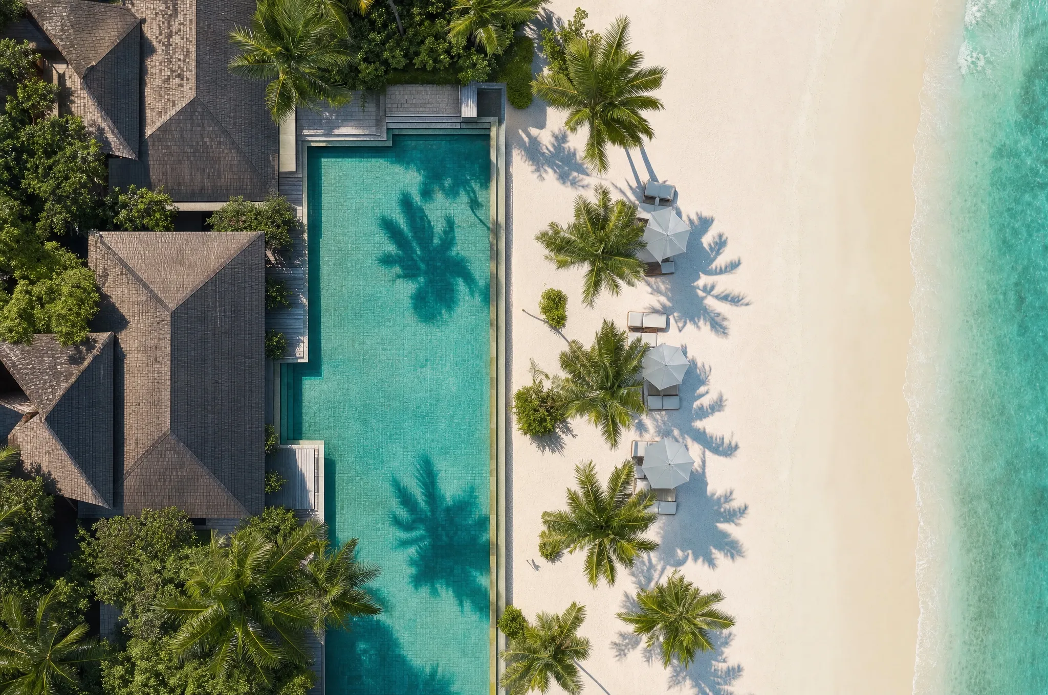 An aerial view of a resort pool with palm trees and sun umbrellas